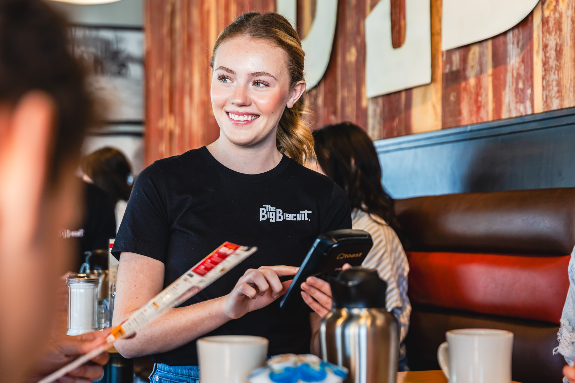 Woman smiling and standing next to dining table with Toast handheld ordering device