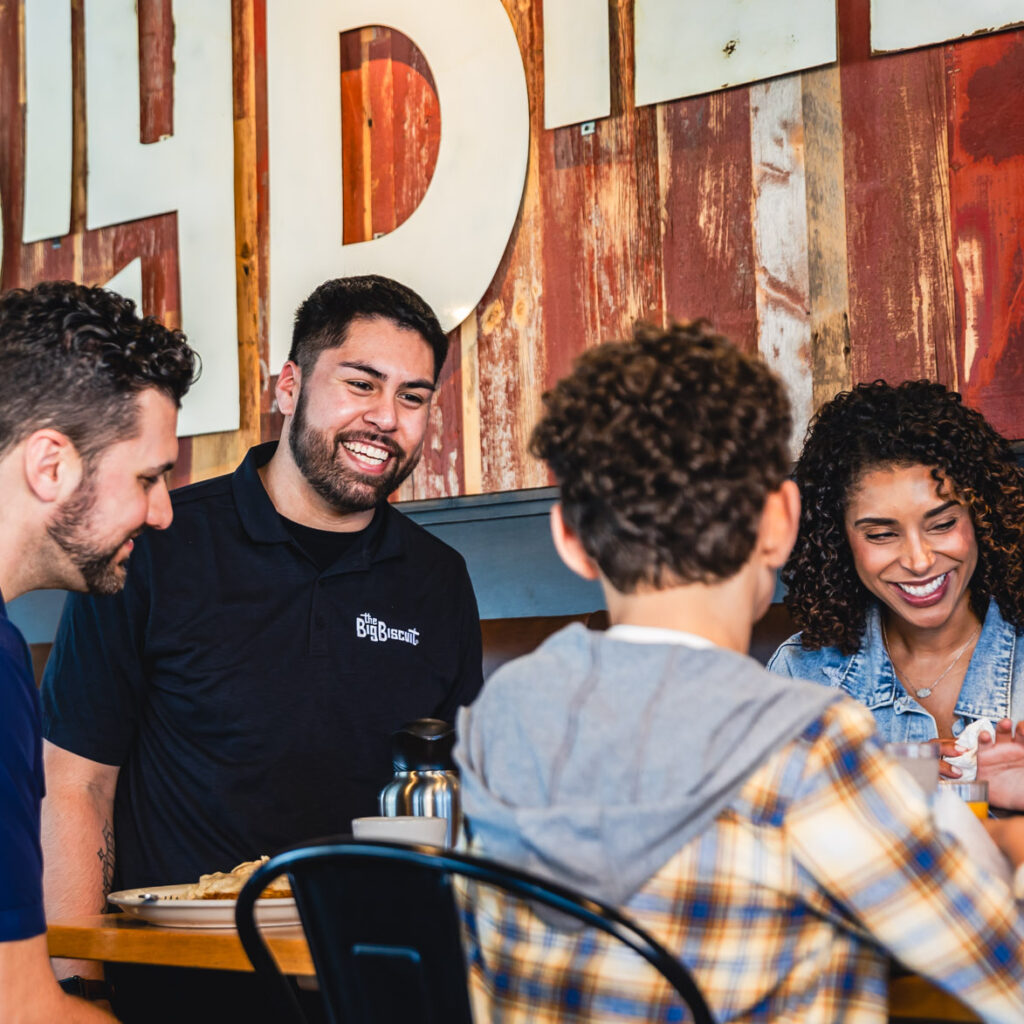 Man smiling and standing beside table with family seated